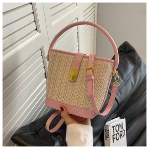 Close-up of woven straw bucket bag featuring pink leather trim and gold metal buckle