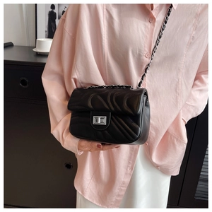 Detail view of wave-pattern quilted crossbody bag with silver rotating lock on a model