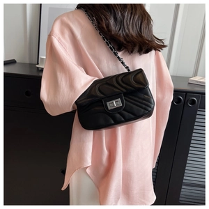 Detail of black quilted leather shoulder bag with silver clasp worn by model in pink shirt