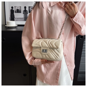 Detail of cream quilted crossbody bag with silver clasp and chain strap on a model