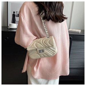 Close-up of cream quilted chain bag with silver twist lock and elegant wavy stitching