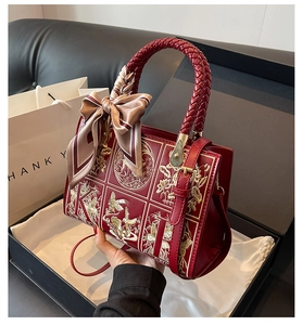 Detail of red leather handbag with gold floral embroidery and silk scarf ornament