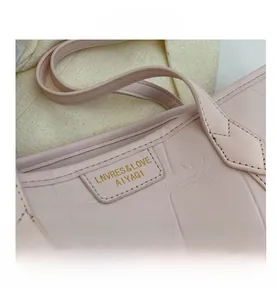 Close-up of pink tote bag with crocodile pattern and golden logo on leather tag