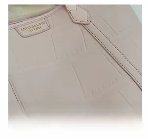 Detailed close-up of light pink faux leather bag with crocodile embossed texture and stitching