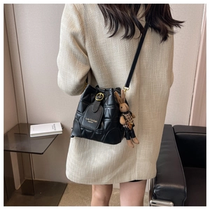 Close-up of black quilted bucket bag with gold logo and cute bunny doll pendant
