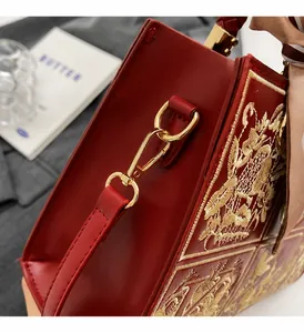 Detail of red crossbody bag featuring gold-tone hardware and silk scarf on handle