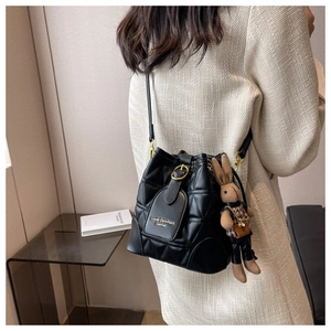 Detail of black quilted bucket bag featuring golden buckle and leopard bunny plush charm