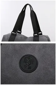 Detail of grey canvas travel bag showing black rounded handles and circular logo patch