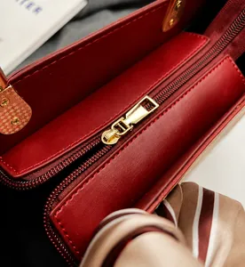 Close-up of red leather handbag featuring gold zipper detail and decorative silk scarf