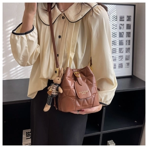 Detail of a brown quilted bucket bag with gold hardware and a cute rabbit charm
