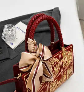 Detail of red crossbody bag with golden embroidery and woven handle with silk scarf