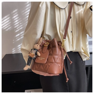 Macro detail of brown leather bucket bag with quilted patterns and rabbit pendant