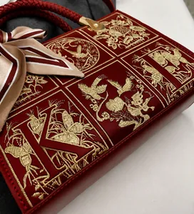 Detailed close-up of red leather handbag with gold embroidery and silk scarf handle