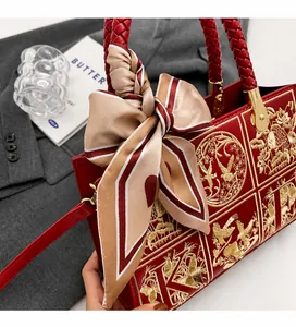 Close-up of dark red crossbody bag featuring gold floral embroidery and a silk scarf handle