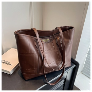Detail of dark brown tote bag with crocodile pattern and golden metal brand label