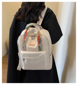 Détail de la broderie florale sur la poignée et logo Sinchaio sur le sac à dos beige