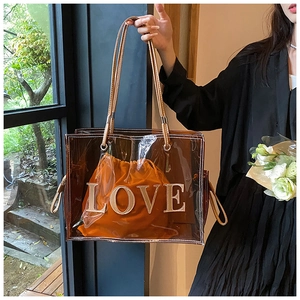 Detailed view of clear PVC tote with an orange 'LOVE' drawstring pouch and leather trim