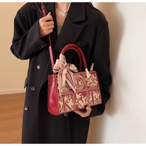 Detailed close-up of red structured handbag with gold embroidery and decorative silk scarf