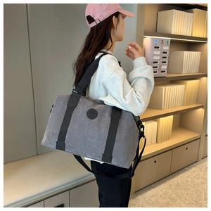 Detail of grey canvas travel bag with black straps worn by model in cozy interior