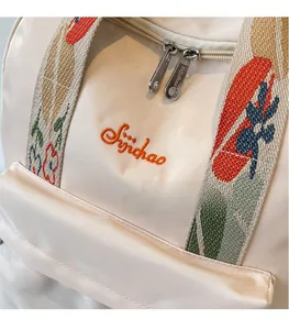 Détail du logo brodé et des bretelles en jacquard sur sac à dos crème texturé