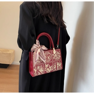 Detail of red leather square handbag with golden bird embroidery and silk scarf handle decoration