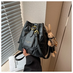 Detail of black quilted bucket bag with gold hardware and a cute bunny bag charm