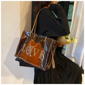 Brown transparent PVC tote bag with LOVE patch shown on shoulder by a model