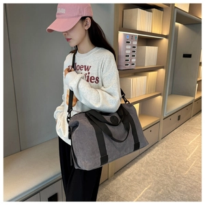 Detail view of large grey canvas travel bag worn as a crossbody by a model in interior