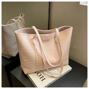 Detail of light pink crocodile pattern embossed tote bag with brand logo on book shelf