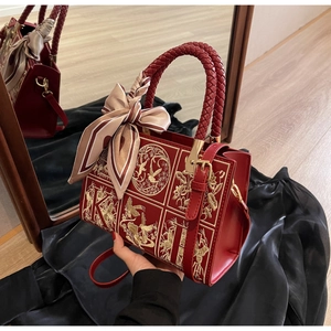 Detailed close-up of red handbag with intricate gold embroidery and decorative silk scarf