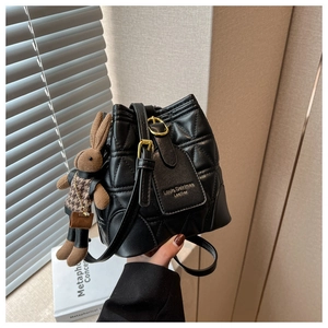 Detail of black quilted bucket bag with golden hardware and cute bunny charm accessory
