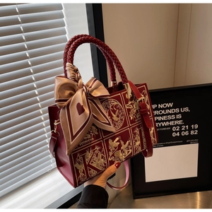 Close-up of burgundy square bag with gold embroidery, woven handle and silk scarf