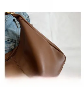 Detail shot of premium brown leather texture and stitching on the minimalist dumpling bag