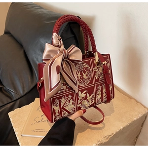 Close-up of red leather handbag with gold embroidery, woven handle and a silk scarf