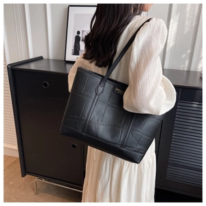 Detailed view of black crocodile embossed tote bag worn with white pleated dress