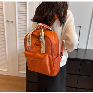 Détail d'un sac à dos en nylon orange avec poignée et bandoulière tissées à fleurs