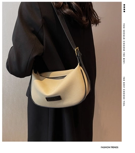 Detail of cream crescent bag featuring black contrast strap and golden metal hardware