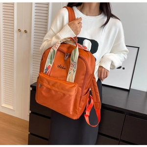 Détail du sac à dos en toile orange avec bretelles brodées et poche avant zippée