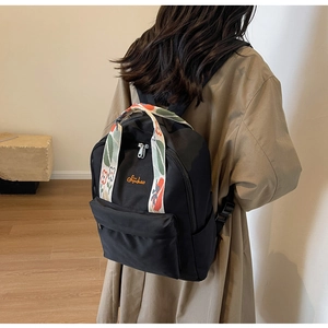 Détail du sac à dos en nylon noir avec poignée brodée de fleurs et broderie orange