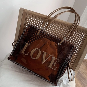 Brown transparent PVC tote bag with LOVE lettering and drawstring pouch on a rattan chair