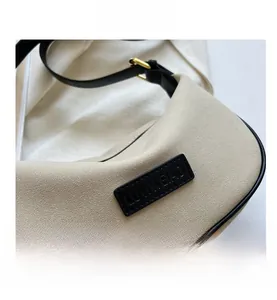Detail of beige hobo bag with embossed black logo plate and golden metal buckle