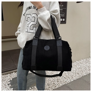 Close-up of black travel bag with round logo, reinforced handles and crossbody strap