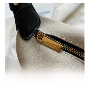 Detailed close-up of smooth golden metal zipper and beige textured fabric on shoulder bag