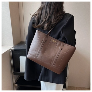 Detail of crocodile-textured brown tote bag with gold logo and slim shoulder strap
