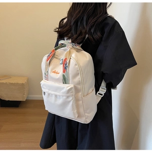 Détail d'un sac à dos en nylon crème avec bretelles florales et logo brodé orange