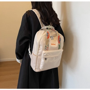 Détail d'un sac à dos en nylon beige avec bretelles à fleurs et logo de marque orange