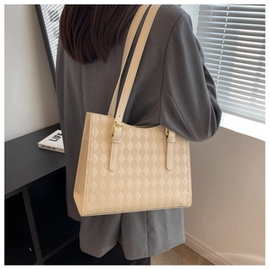 Rear view of a beige quilted tote bag with adjustable straps worn by a female model