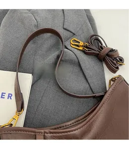 Detail of dark brown leather handbag featuring a gold buckle and adjustable shoulder strap