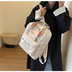 Détail du sac à dos en toile crème avec broderie orange et bretelles jacquard colorées