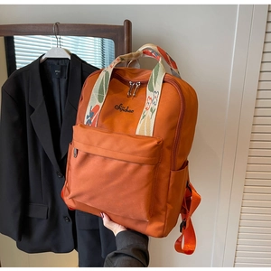 Détail du sac à dos orange montrant la poignée à fleurs et le logo brodé